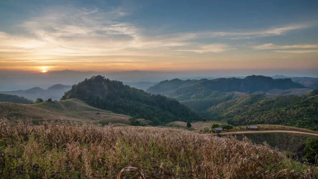 Soleil bas sur les champs et les collines boisées de Doi Samer Dao, avec des montagnes qui s’estompent dans la brume.