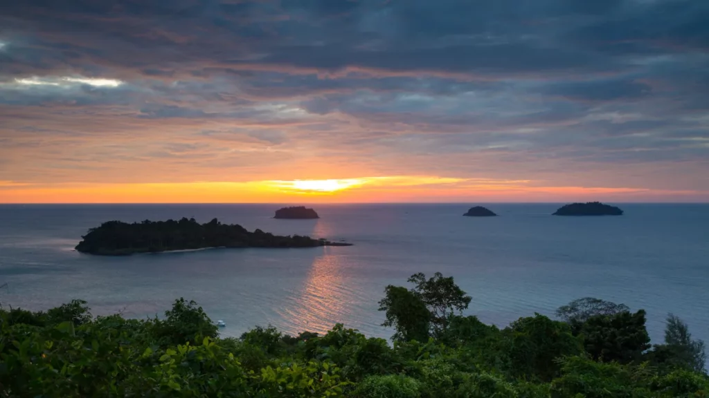 Soleil bas au-dessus de la mer près de Ko Chang, avec plusieurs îlots à l’horizon et une végétation dense au premier plan.