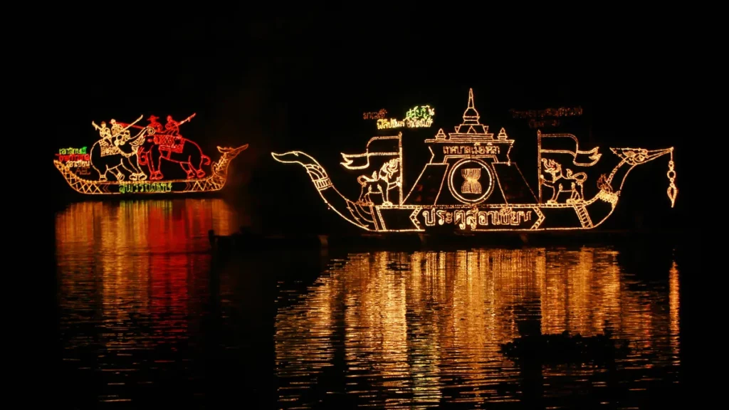 Bateaux décorés de motifs lumineux dorés et rouges sur le Mékong pendant Lai Reua Fai, avec leurs reflets dans l’eau sombre.