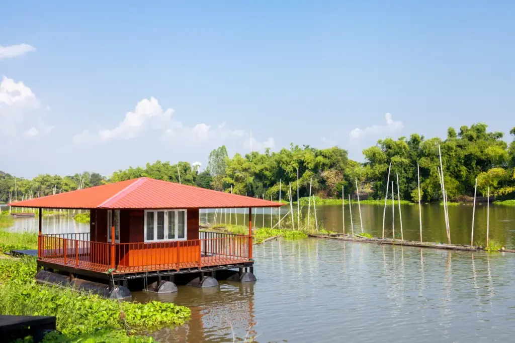 Klein rood houten drijvend huis op de Sakae Krang-rivier, omringd door waterplanten.