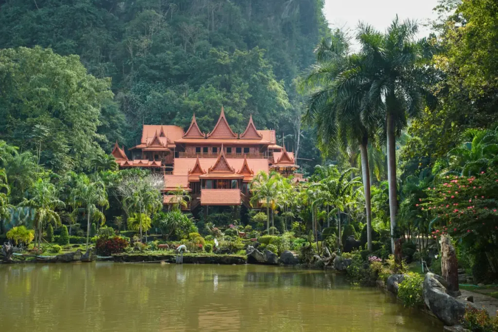 Traditionele houten tempel van Wat Tham Khao Wong, omringd door palmbomen en een grote vijver.